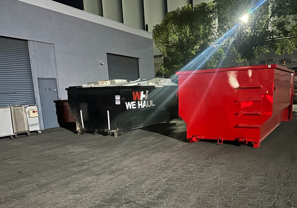 Nighttime view of two red dumpsters located in a parking lot, illuminated by faint ambient light.