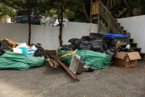 Piled garbage bags and trash clutter a residential driveway, indicating a need for waste collection.